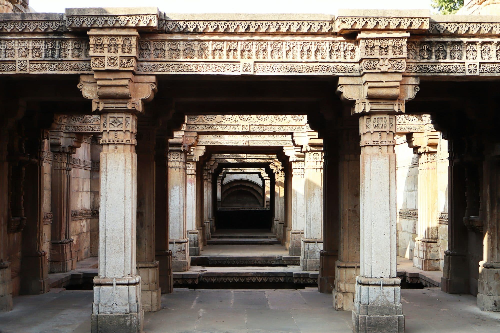 Carved sandstone pillars and lintels of the Adalaj stepwell near Ahmedabad, framing a corridor of colonnades that steps down into the well