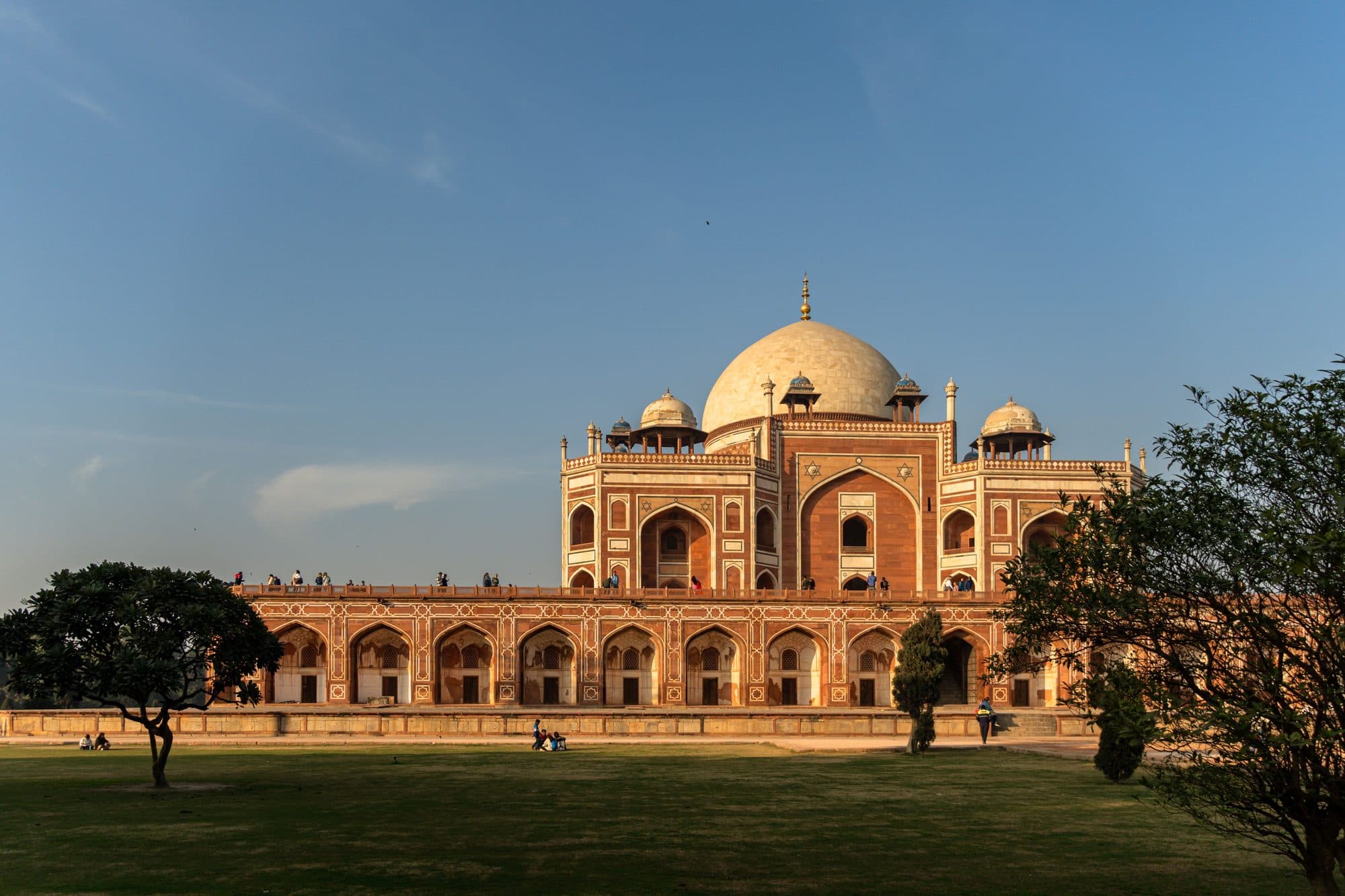 Humayun's Tomb in Delhi, its red sandstone facade and white marble dome glowing in warm early-morning light, seen across the garden lawn