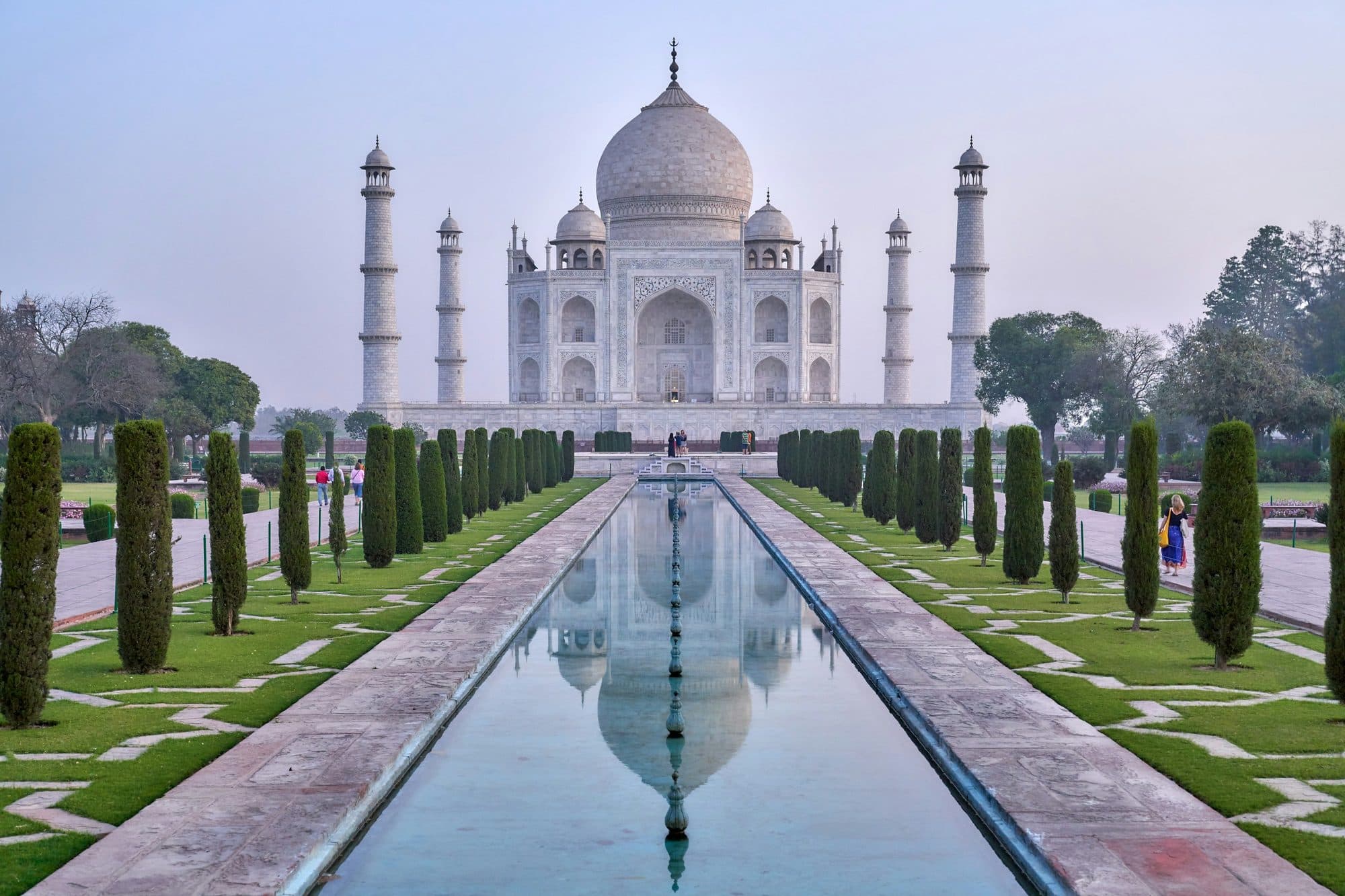 The Taj Mahal in Agra reflected in the long garden pool lined with cypress trees, seen from the central axis in soft early-morning light