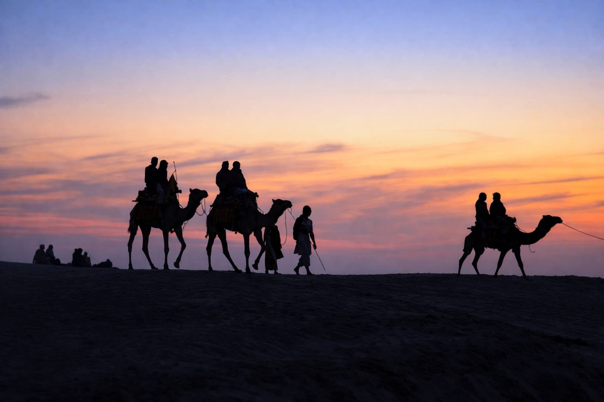 Camel riders silhouetted on a sand dune at sunset in the Thar Desert near Jaisalmer
