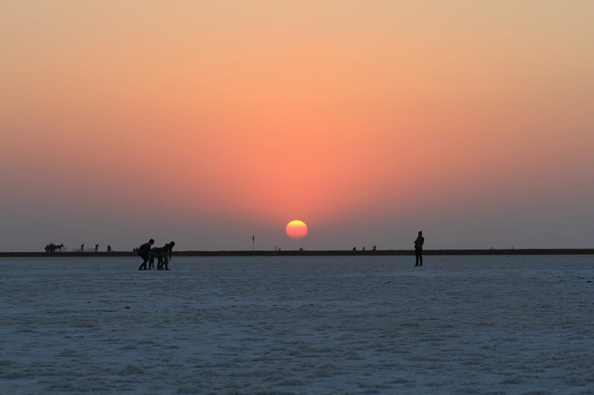 Sunset over the White Rann of Kutch, with the sun low above the flat salt desert and a few visitors silhouetted on the horizon